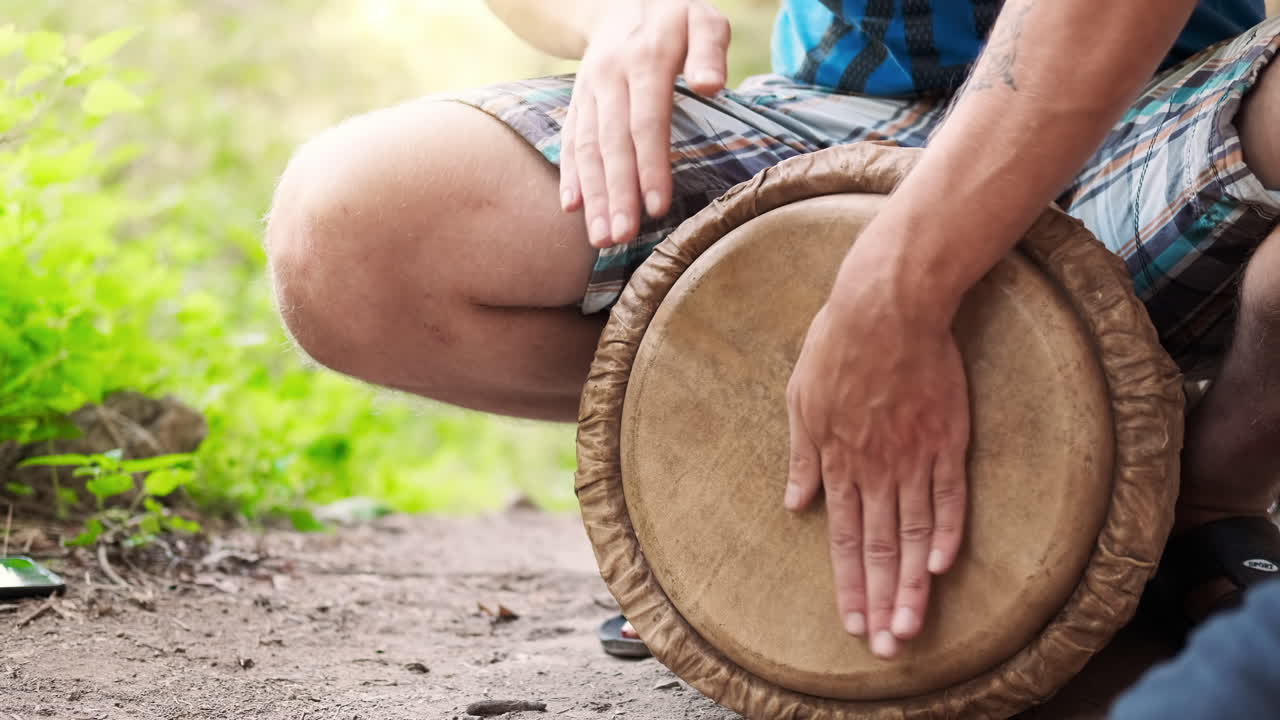 A man playing ethnic drums while sitting on the ground in the nature