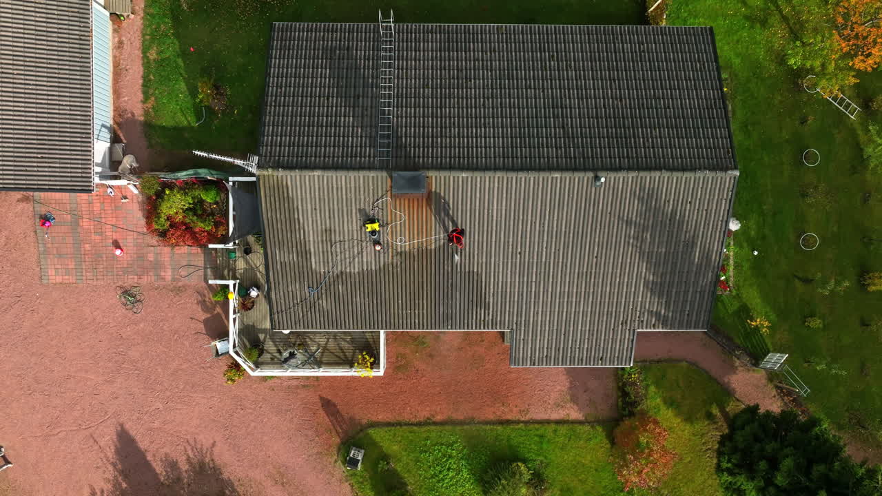 Top down drone shot above a person pressure washing a house roof, autumn day