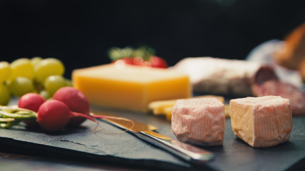 Moving down to a close shot of cheese on a garden table showcasing an assortment of snacks including salami and bread. Great for food vlogs, recipe videos, and appetizing product presentations