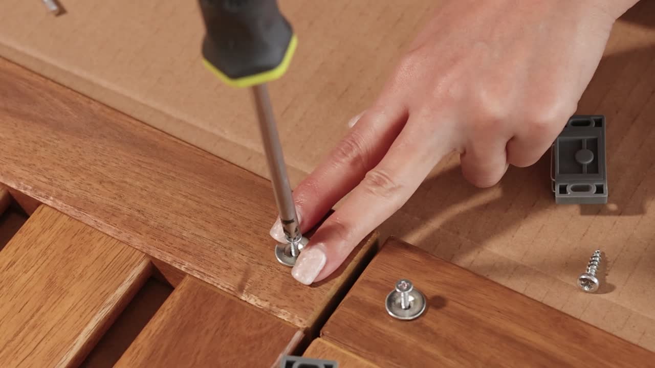 Detailed close-up of hands precisely tightening screws into wooden panels during furniture assembly