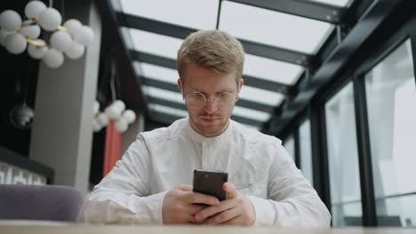 handsome-man-is-waiting-order-in-cafe-and-using-internet-in-smartphone-social-media-addiction-and-doomsurfing