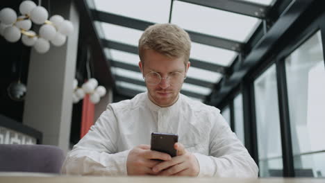 handsome man is waiting order in cafe and using internet in smartphone social media addiction and doomsurfing