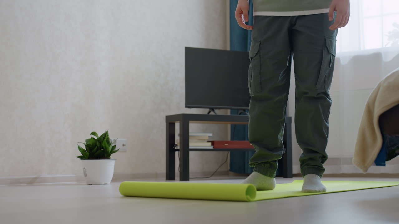 Close up of bright green fitness mat slightly curled on light wooden floor inside room, suggesting end of exercise session or beginning of clean-up, highlighting texture and color in soft daylight