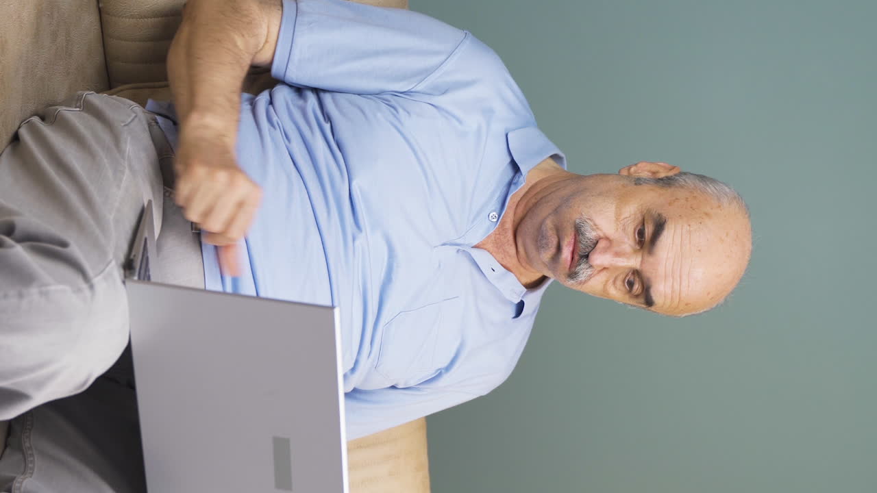 video vertical de un anciano viendo una película en una computadora portátil con una expresión feliz.