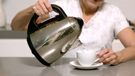 mujer vertiendo agua hirviendo de la tetera en la taza