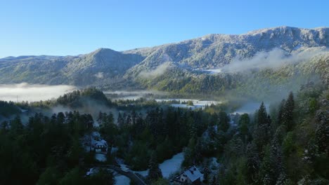 Aerial-breathtaking-view-of-a-snow-capped-mountain-towering-over-a-mist-enshrouded-forest-and-valley