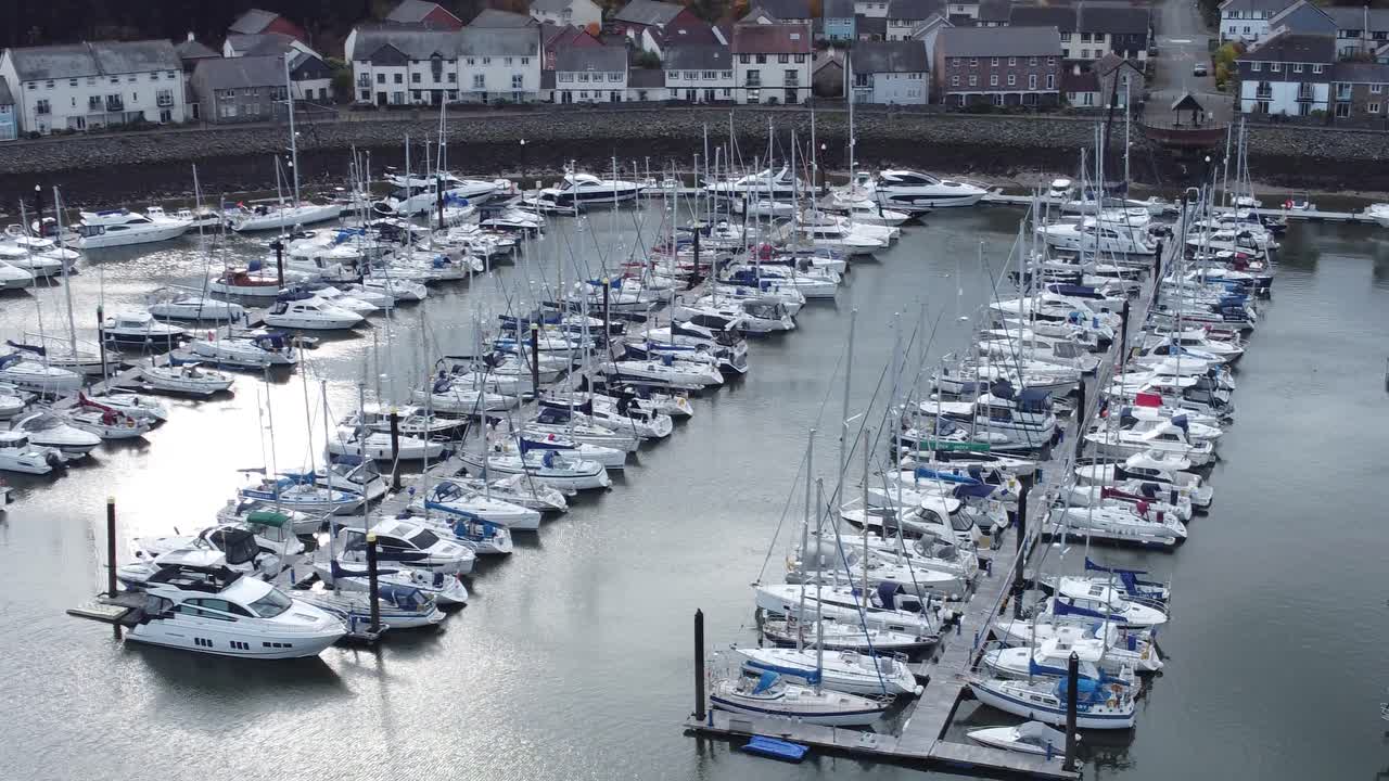 Naturskjønt luftfoto av en luksuriøs havnelandsby med leiligheter, yachter og seilbåter langs en fjellkystlinje, synkende fremover.