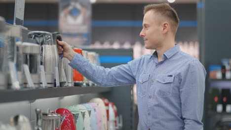 young handsome man chooses an electric kettle to buy. inspects the device, examines the price tags and the characteristics of the model.