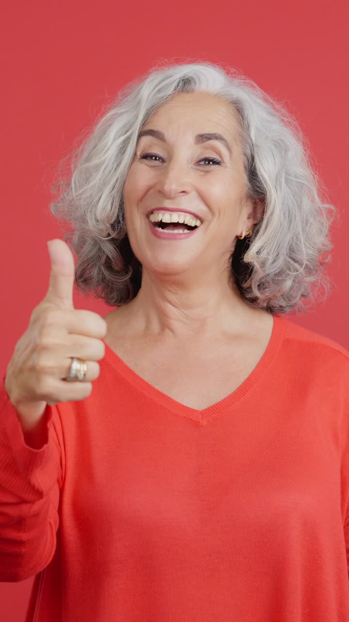 Happy Senior Woman Giving Thumbs Up on Red Background
