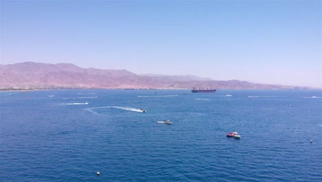 aerial view of recreational boats and jet skis on the sea with a distant port and mountains