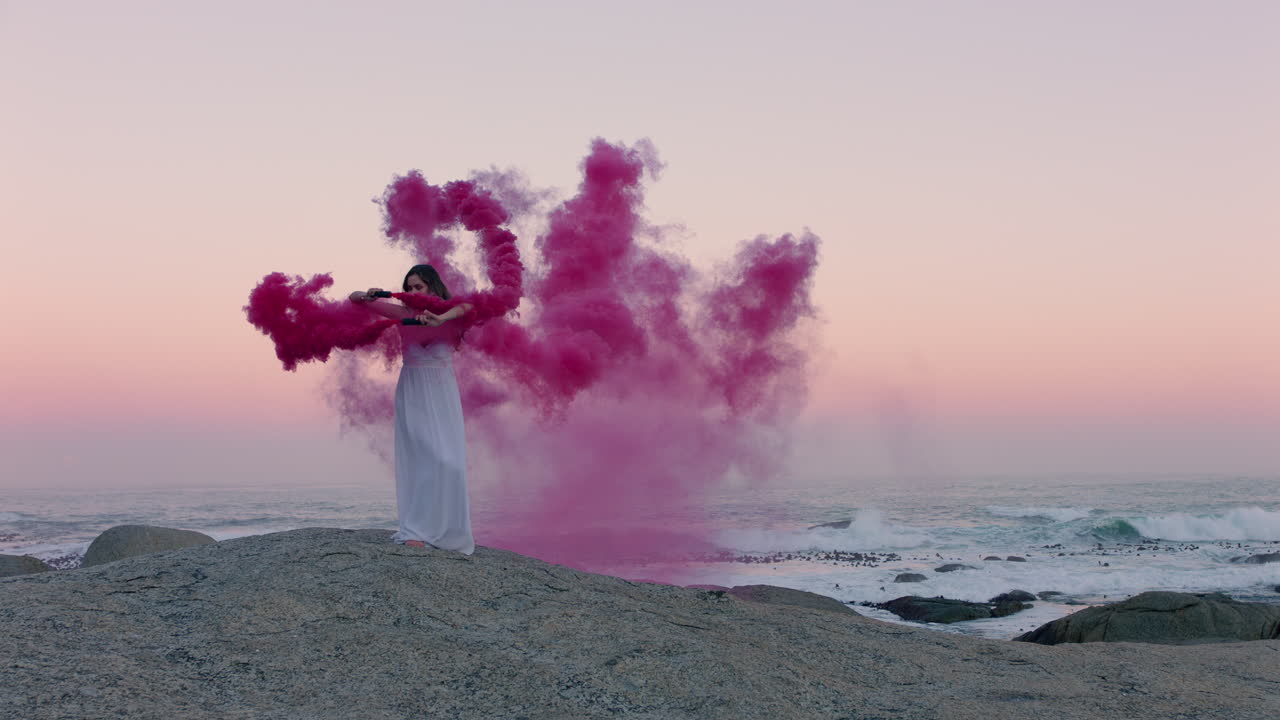mujer con una bomba de humo rosa bailando en la playa temprano en la mañana celebrando la libertad creativa