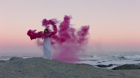 woman-holding-pink-smoke-bomb-dancing-on-beach-in-early-morning-celebrating-creative-freedom