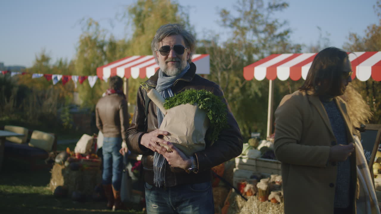 Mature Man in Sunglasses Posing with Bag Mature Man in Sunglasses Posing with Bag of Fruits or Vegetables and Looks at Camera Shops on Farmers Market Buys Fresh Products and Takes Care about Health