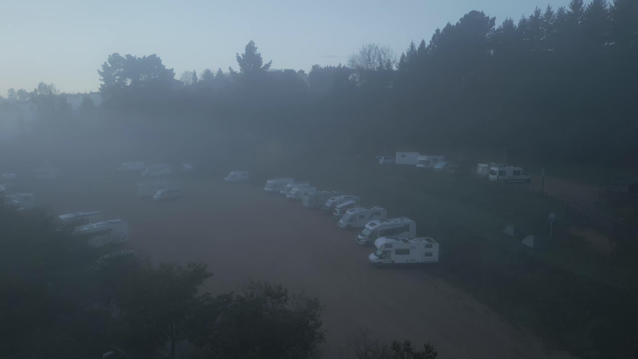 Overhead aerial perspective revealing camping vehicles nestled among misty trees during early morning, depicting peaceful wilderness retreat and tranquil travel lifestyle