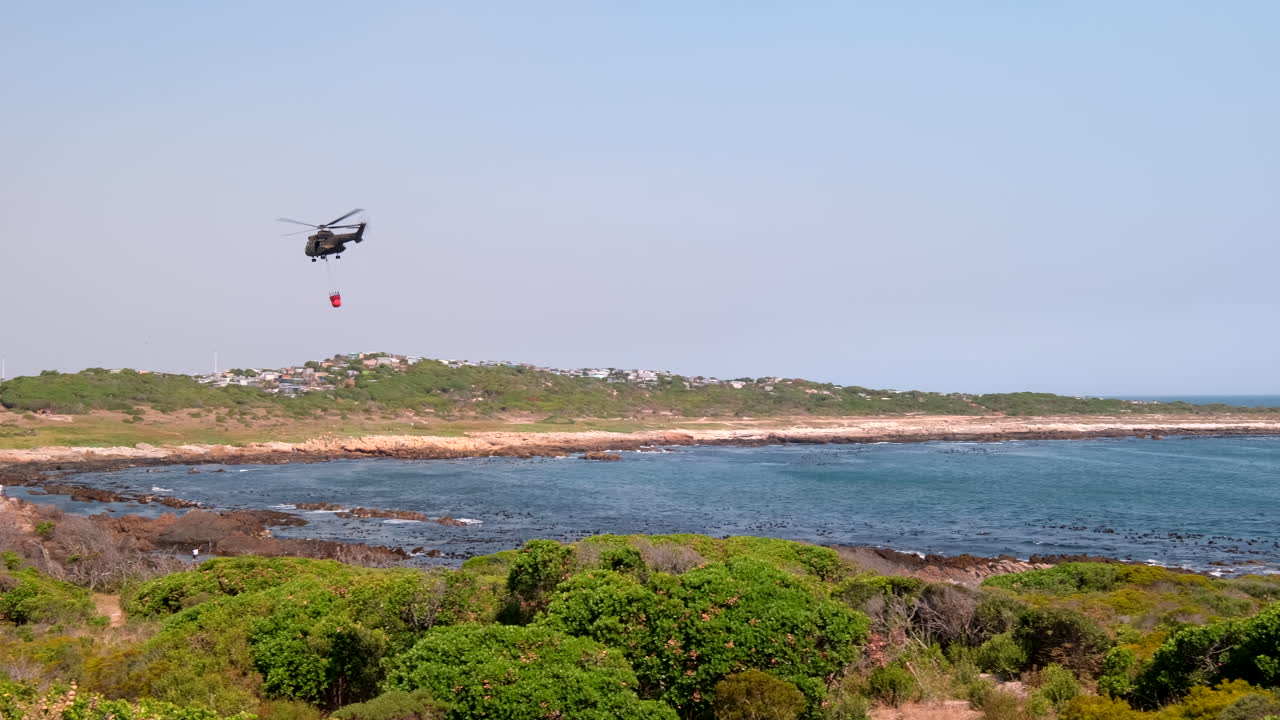 Helikopter terbang menumpahkan air laut ke kebakaran hutan menggunakan helibucket, gerak lambat