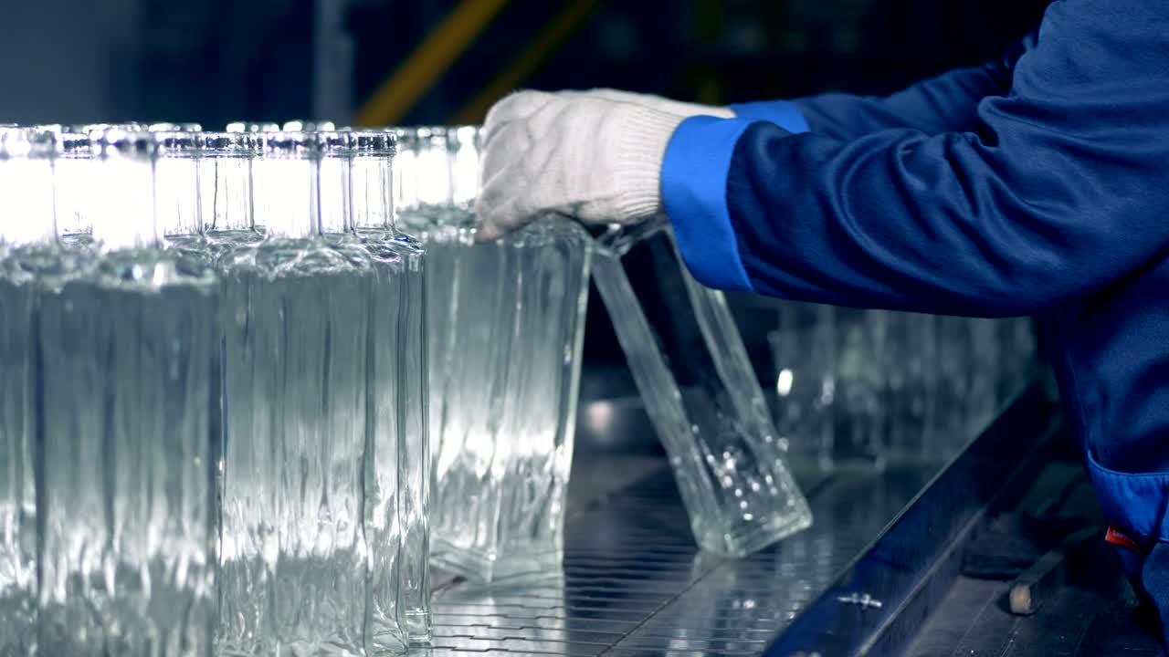 Glass-house employee is moving glass bottles along the transporter
