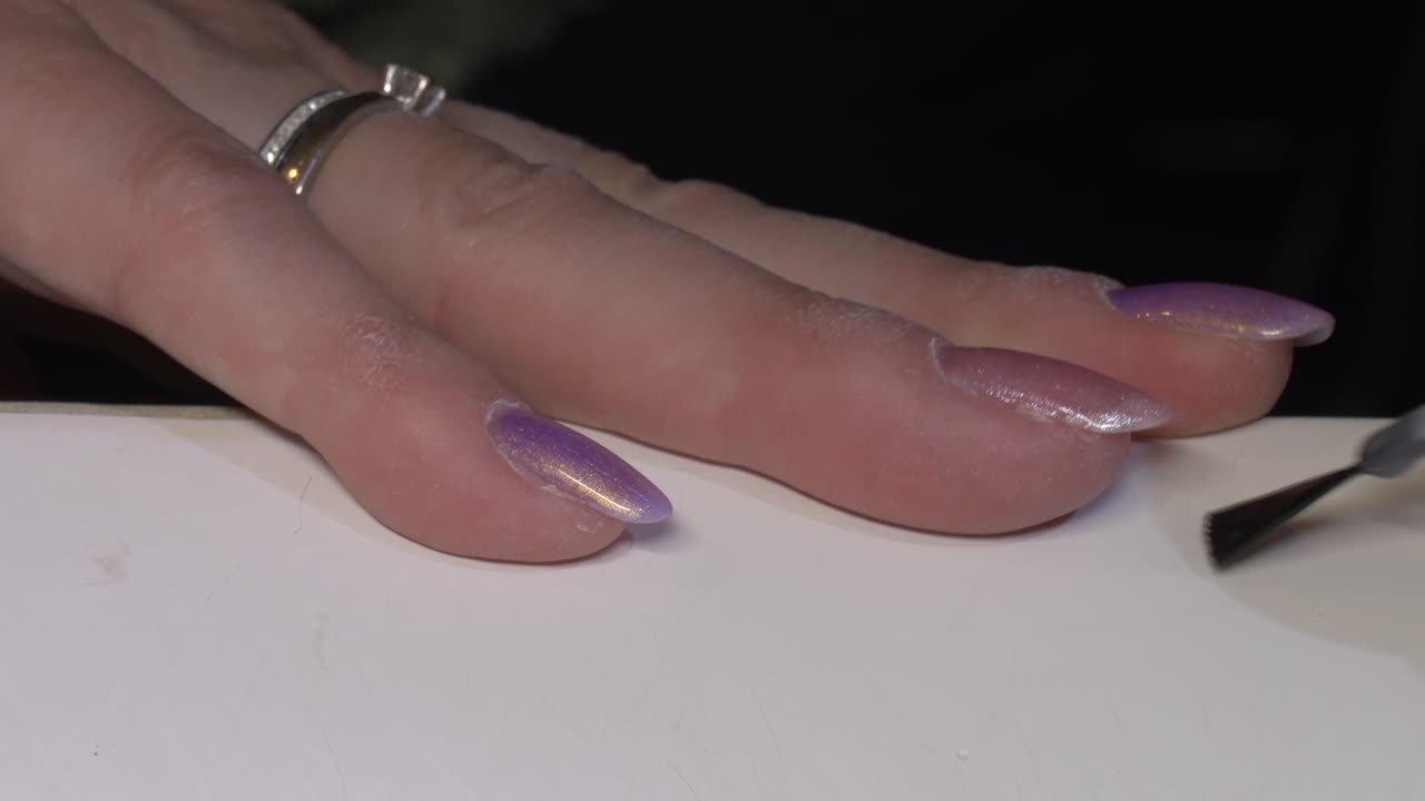 CLose up shot of woman apply purple pink glitter Nail Polish on finger
