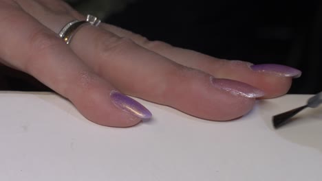disparo de cerca de la mujer aplicar esmalte de uñas de brillo rosa púrpura en el dedo