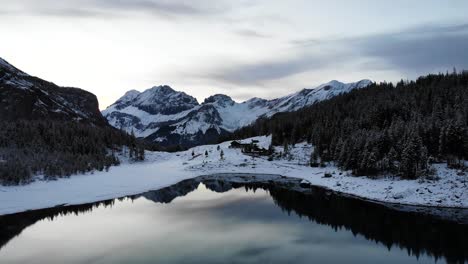 Aerial-flyover-over-lake-Oeschinensee-in-Kandersteg,-Switzerland-with-reflection-of-peaks-on-a-winter-day