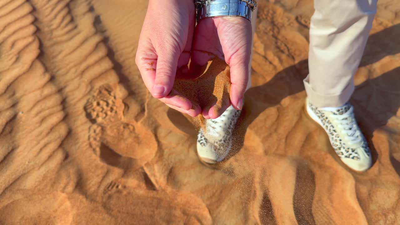 Händer med vit hud som håller i ökensand under en safariutflykt i Dubai