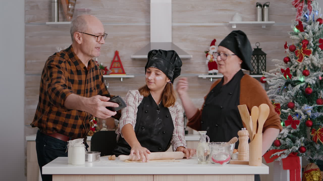 손녀가 테이블에 서서 롤링 핀을 사용하여 집에서 만든 쿠키 반죽을 만들고 있습니다.