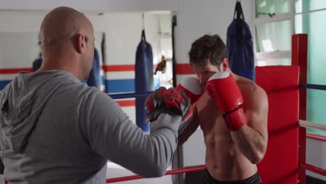 hombre caucásico entrenando con el entrenador en el ring de boxeo