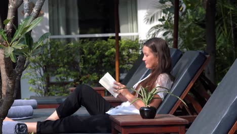 young lady relaxing on a sun lounger by the pool reading a book at a tropical hotel