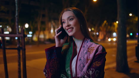 mujer alegre contestando la llamada de pie ciudad nocturna de cerca. chica hablando por teléfono