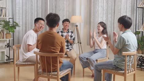아시안 십대 그룹이 의자에 앉아 집에서 원을 형성합니다. 축하, 박수 또는 박수를 치고 있습니다.