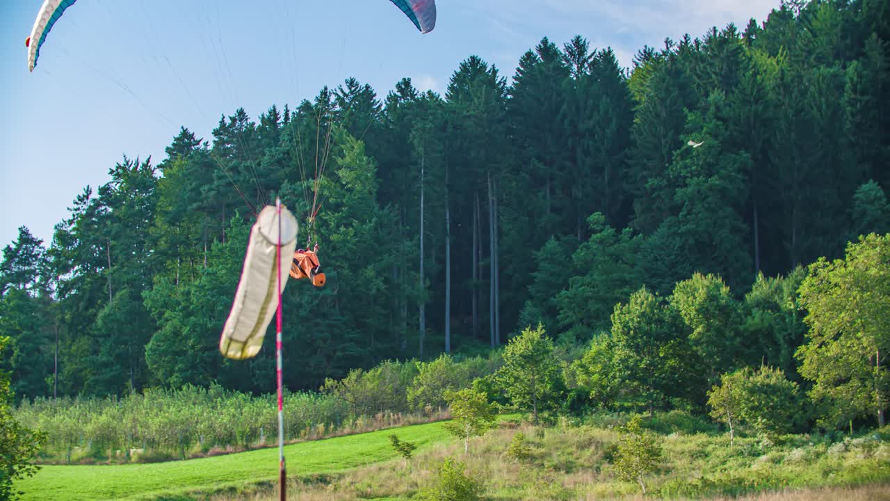 Man paragliding slightly above the ground in the forest during a bright sunny day. Handheld tracking shot from the viewer perspective