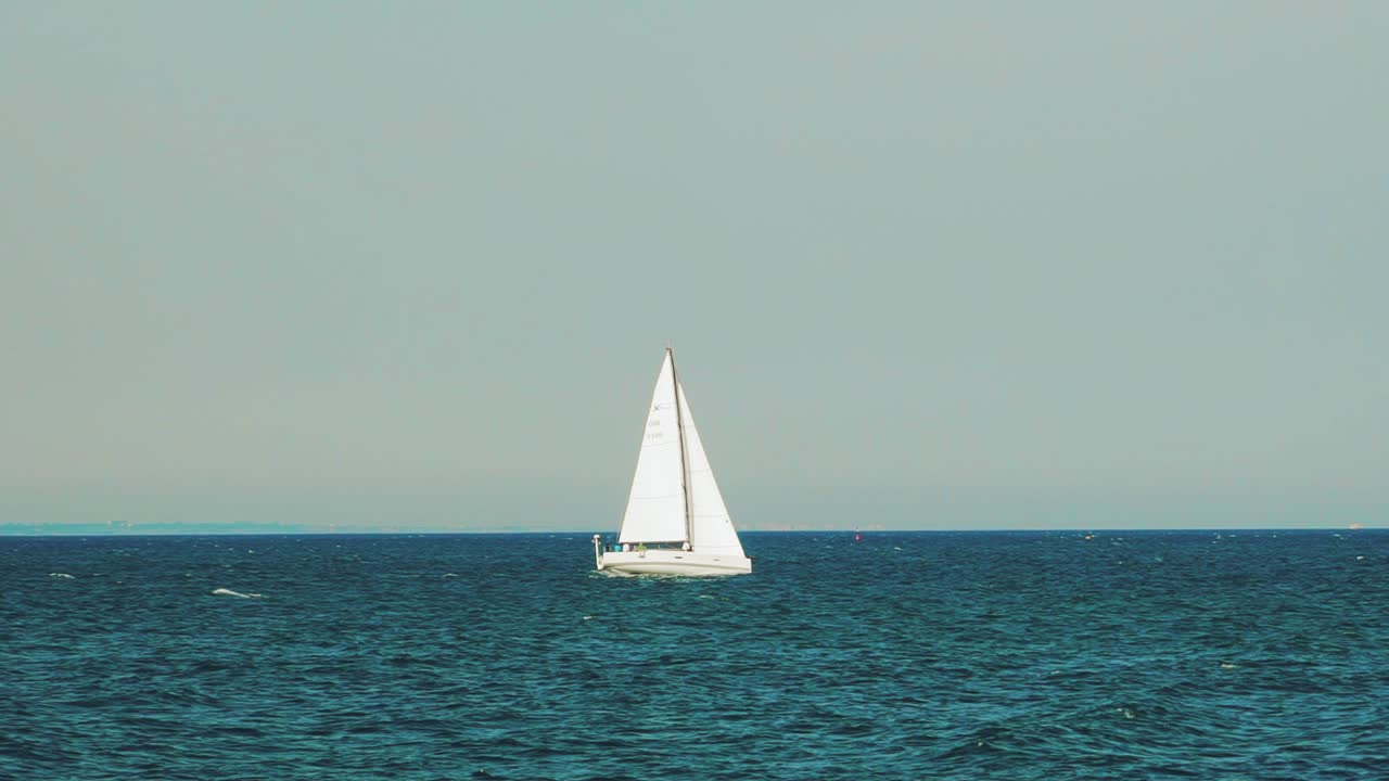 white sailboat is sailing on the sea far from the coast in the summer. Slow motion