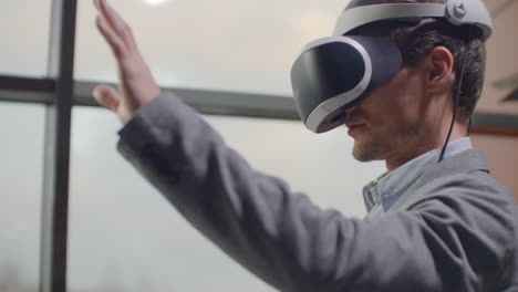 man in a helmet of virtual reality against the background of a huge window in the office at the workplace. design engineer working in a virtual reality helmet.