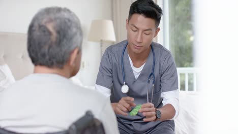 diverse male doctor and senior male patient in wheelchair discussing medication at home, slow motion