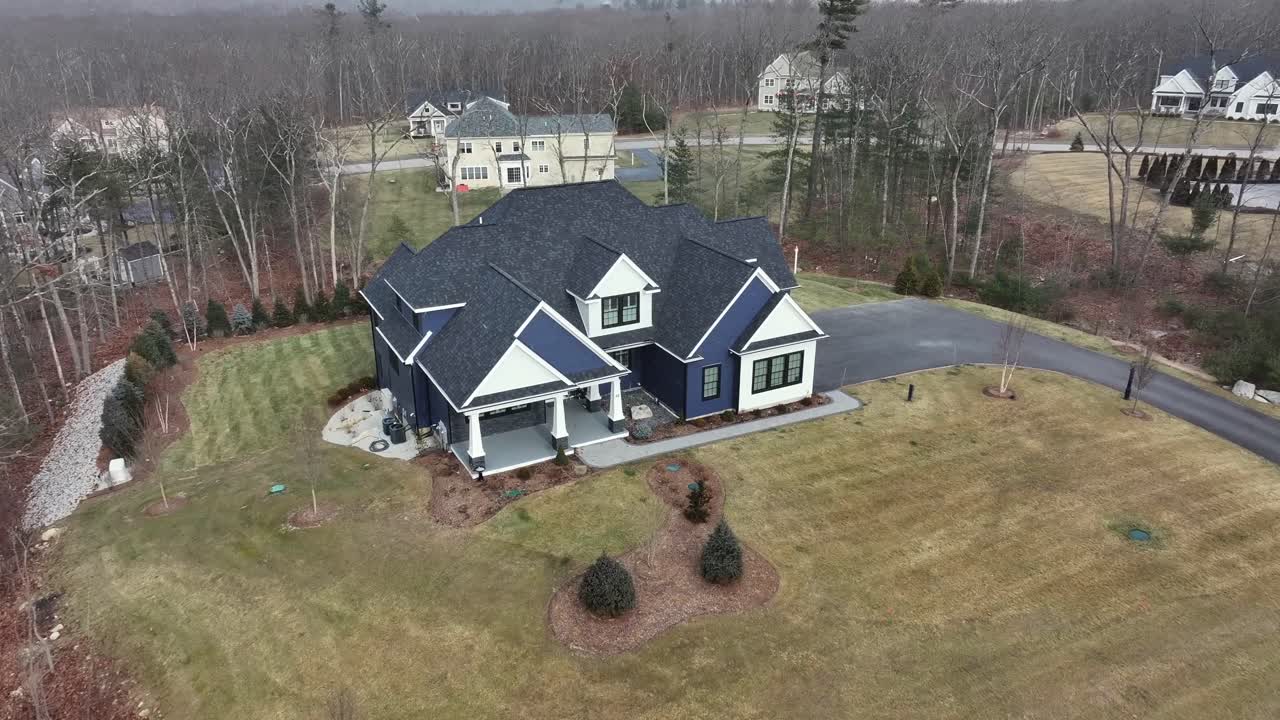 American villa in suburb of american town in winter season. Flying snow flurries from sky. Black roof and white facade of building. Luxury large real estate in USA, Massachusetts.