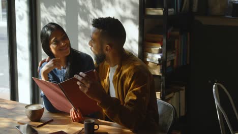 Front-view-of-young-mixed-race-couple-discussing-over-menu-card-in-cafe-4k