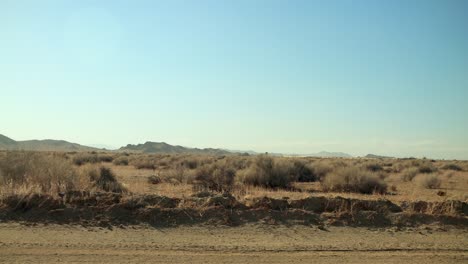 Conduciendo-Lentamente-Por-Un-Camino-De-Tierra-En-Medio-Del-Desierto-Con-Montañas-En-La-Distancia-Y-Arbustos-Secos-Pasando