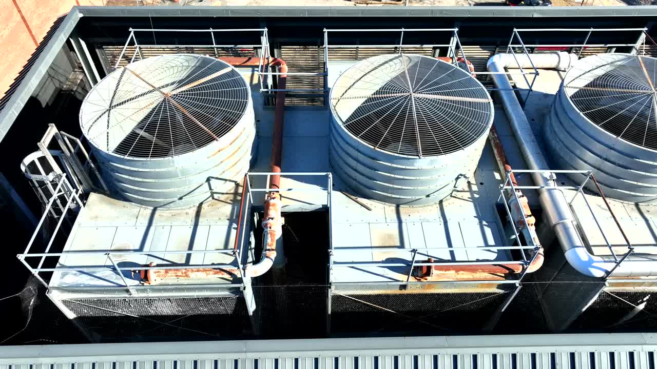 Top-down aerial view of an industrial HVAC cooling system installed on a rooftop. The setup features multiple cylindrical cooling towers and connecting pipes