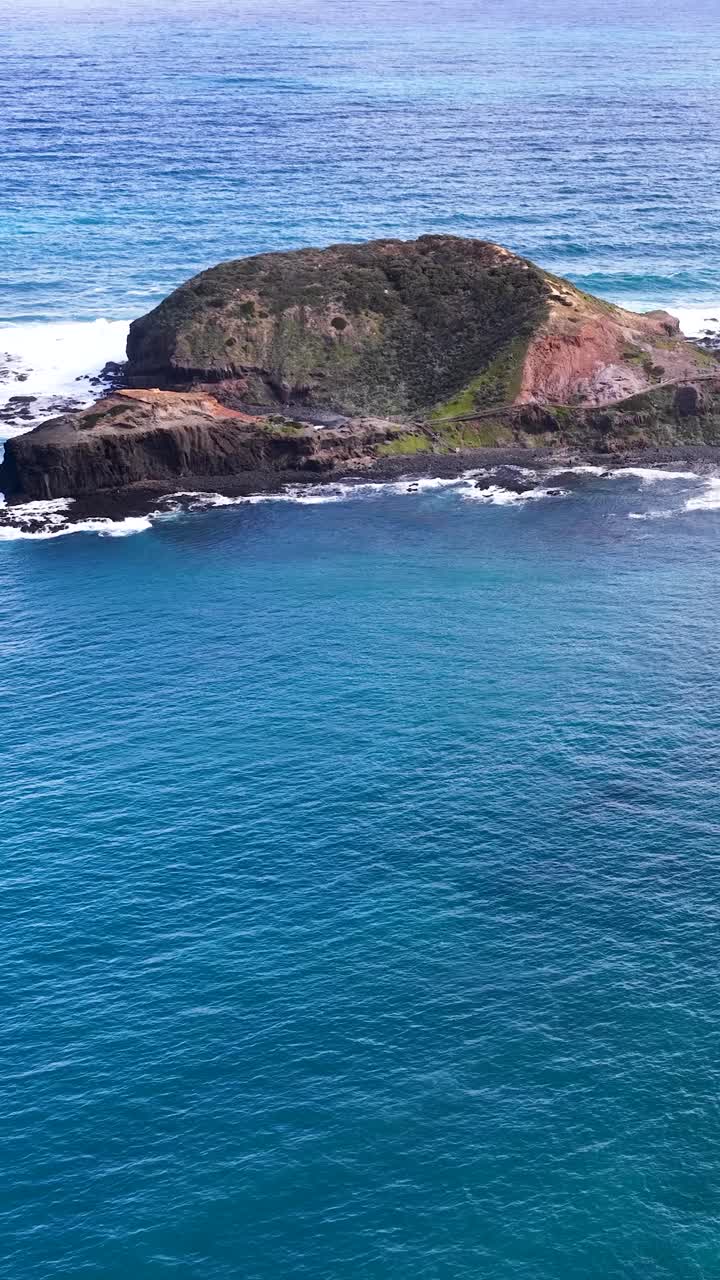 Una telecamera drone si avvicina dolcemente a un'isola aspra, rivelando l'oceano blu, scogliere rocciose e vegetazione costiera.