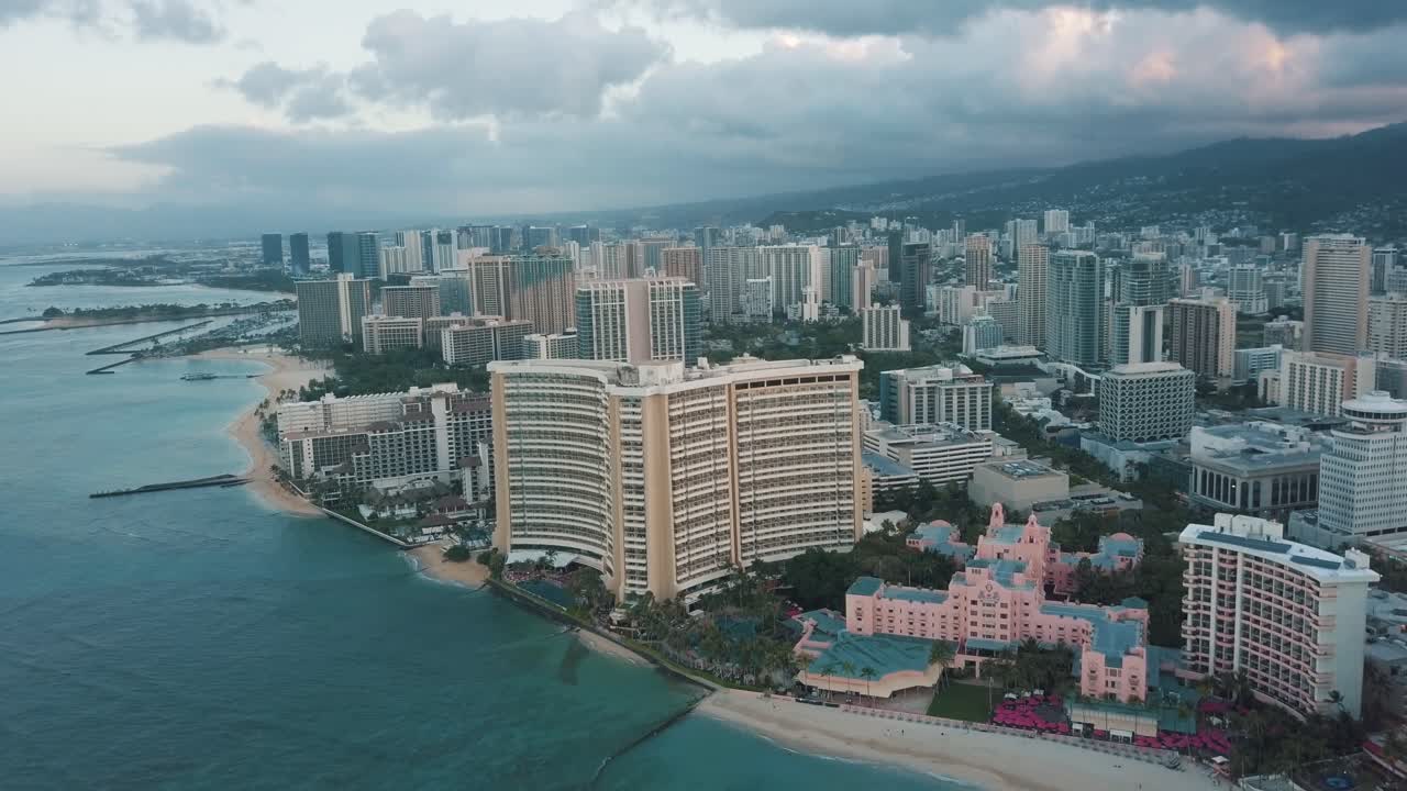 Drone aereo in lenta panoramica che sorvola lo skyline colorato di Honolulu al tramonto a Oahu, Hawaii, con la spiaggia di Waikiki come punto di interesse speciale