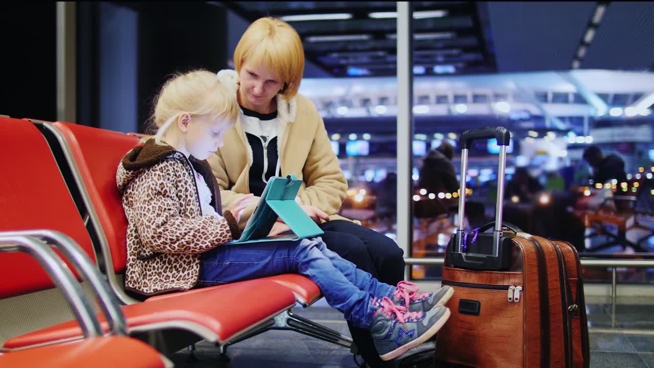madre e hija esperando su vuelo niña jugando en una tableta