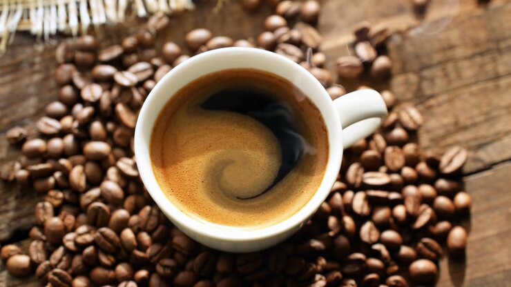 Dampfender heißer Kaffee in weißer Tasse mit gerösteten Bohnen auf Holztisch