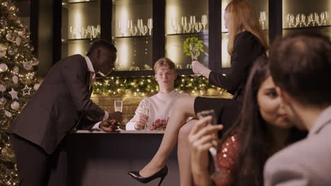 grupo de amigos celebrando la fiesta de año nuevo, una pareja se besa, mientras los demás están en el bar comiendo uvas y hablando