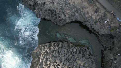 tourist man swims in shallow billabong as ocean waves crash onto rocks