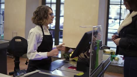 Smiling-woman-customer-paying-with-her-EC-card-at-supermarket-checkout-and-taking-her-brown-paper-bag-with-products-from-the