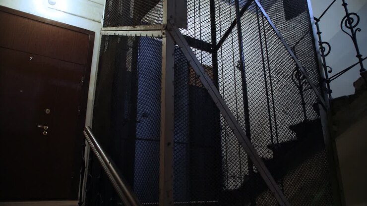 Old wooden elevator ascends in metal shaft in building with staircase