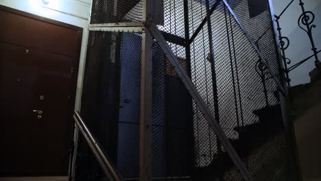 old wooden elevator ascends in metal shaft in building with staircase