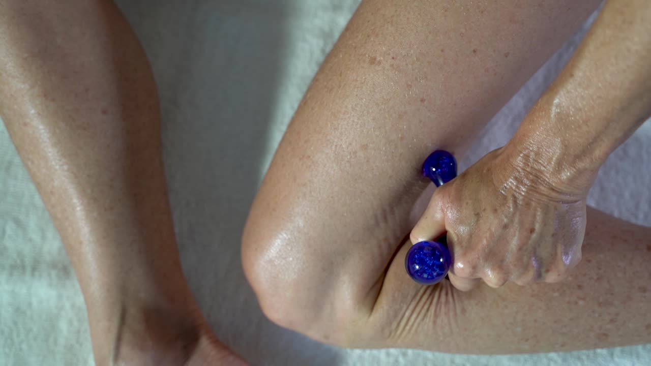 Ekstremt nærbillede af en kvinde, der bruger et massageværktøj til at lægge pres på triggerpunkterne på sit ben