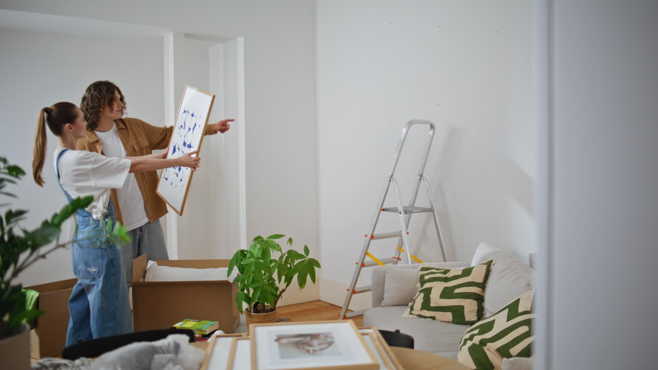 Couple choosing picture place on wall living room. Husband helping decorate