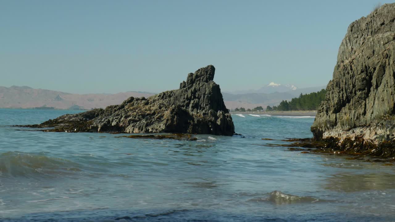 Coastal Majesty: A dramatic rock formation stands amidst the sea, framed by majestic snowy mountains