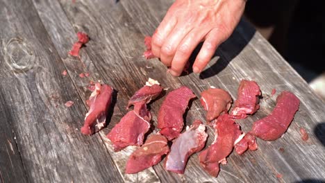 male hand organizing raw boneless deer meat filet on wooden table - sunny outdoor nature clip in slow motion